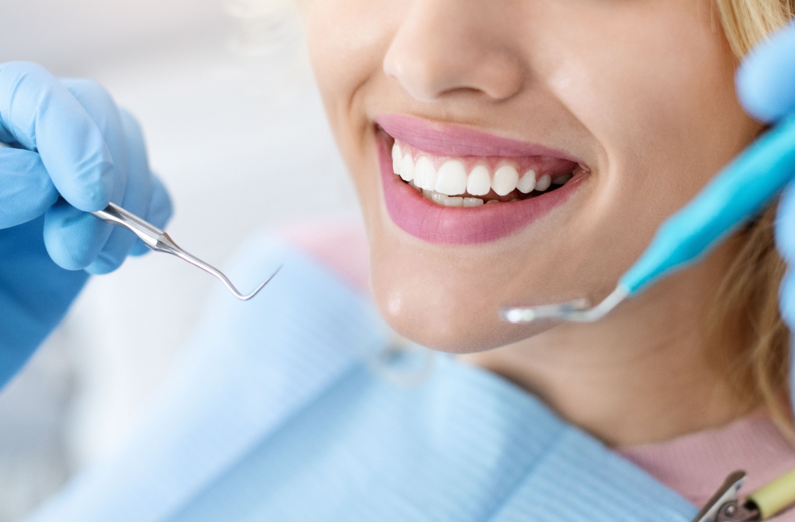 Close-up of a patient smiling after a whitening treatment with dental tools visible near their mouth.