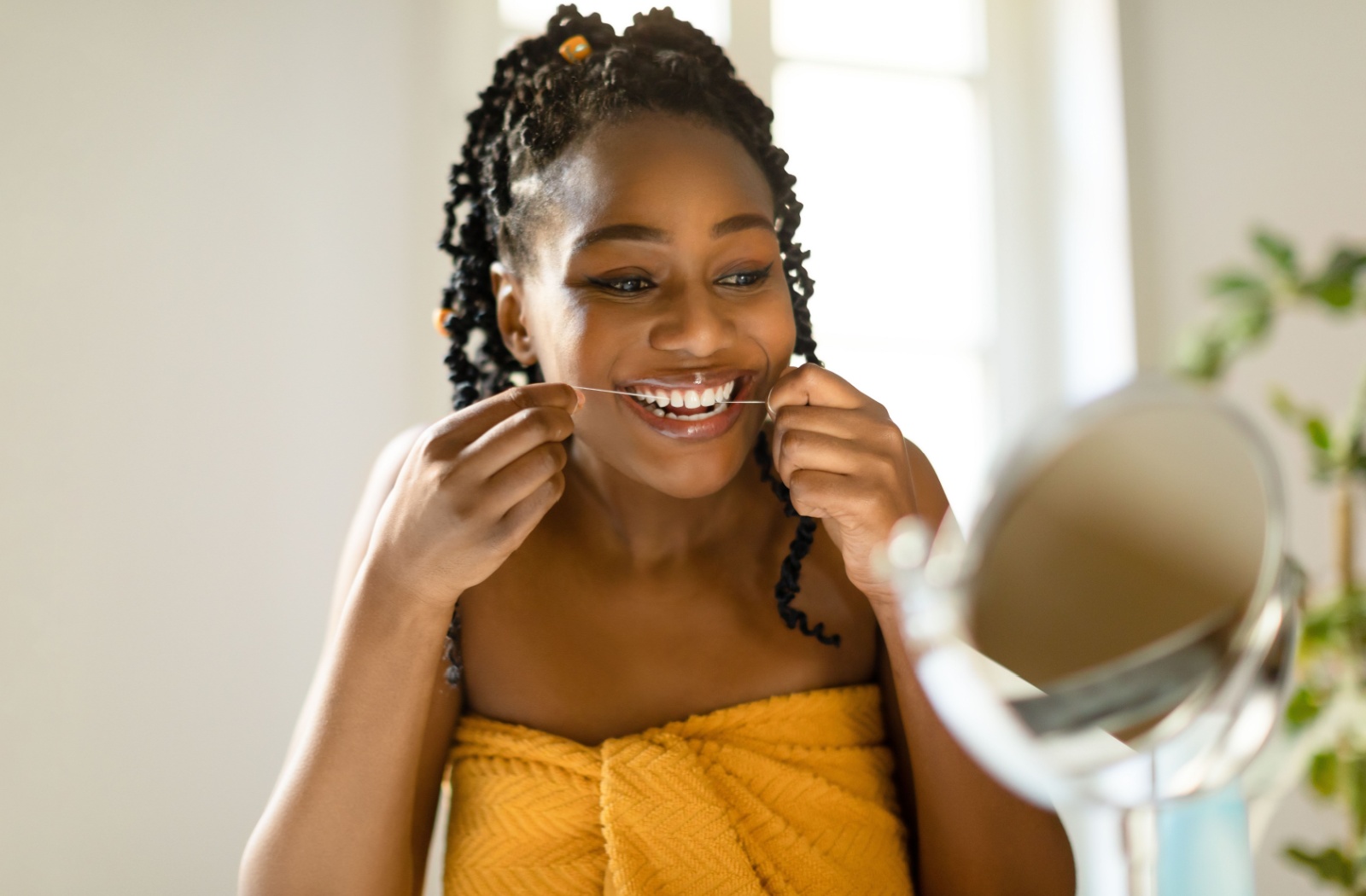 Person smiling while flossing their teeth in a bathroom mirror.
