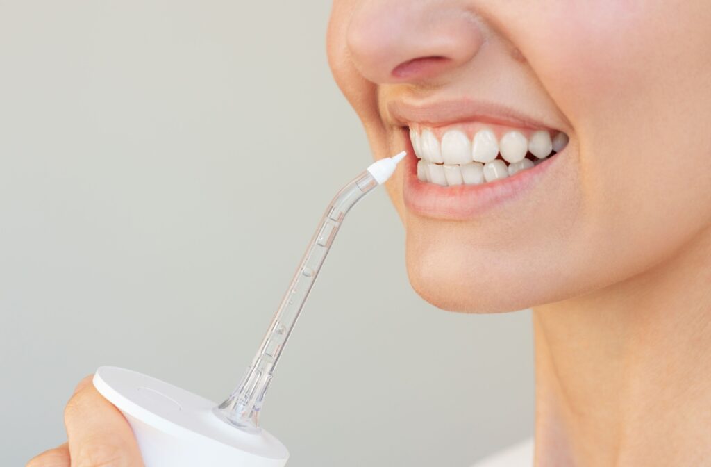 Close-up of a smiling person using a water flosser on their teeth.