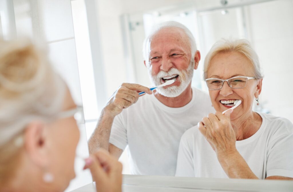 Two people brushing their teeth while looking in the mirror to help prevent gum disease.